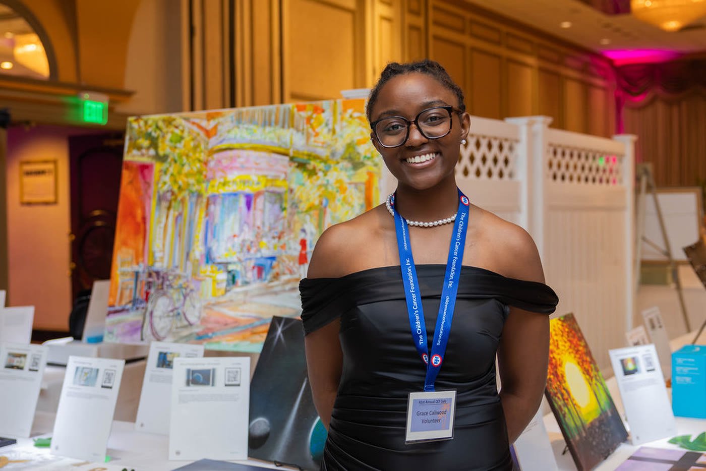 A young guest beside a display of paintings at a gala