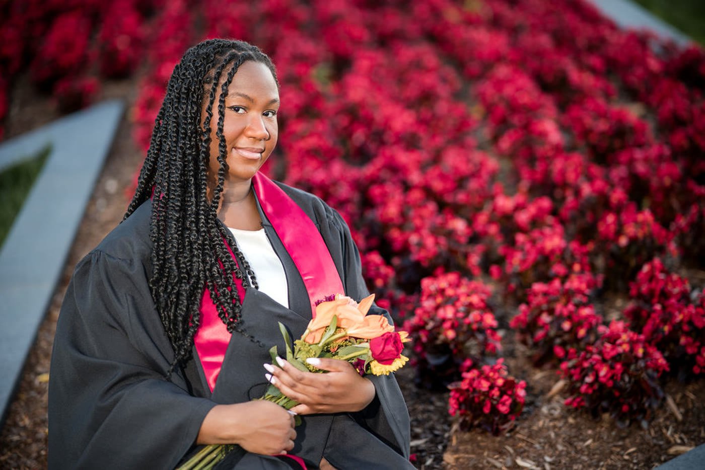 Graduate holding flowers in front of bright red blossoms