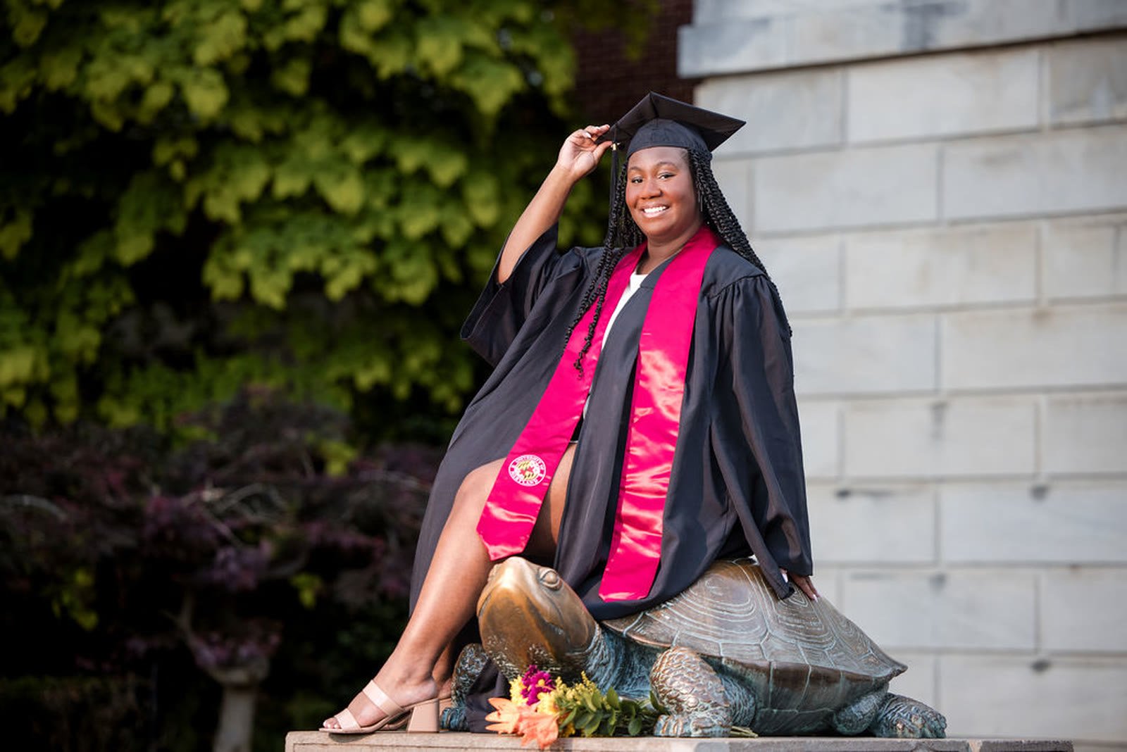Graduate seated on the campus turtle statue in cap and gown